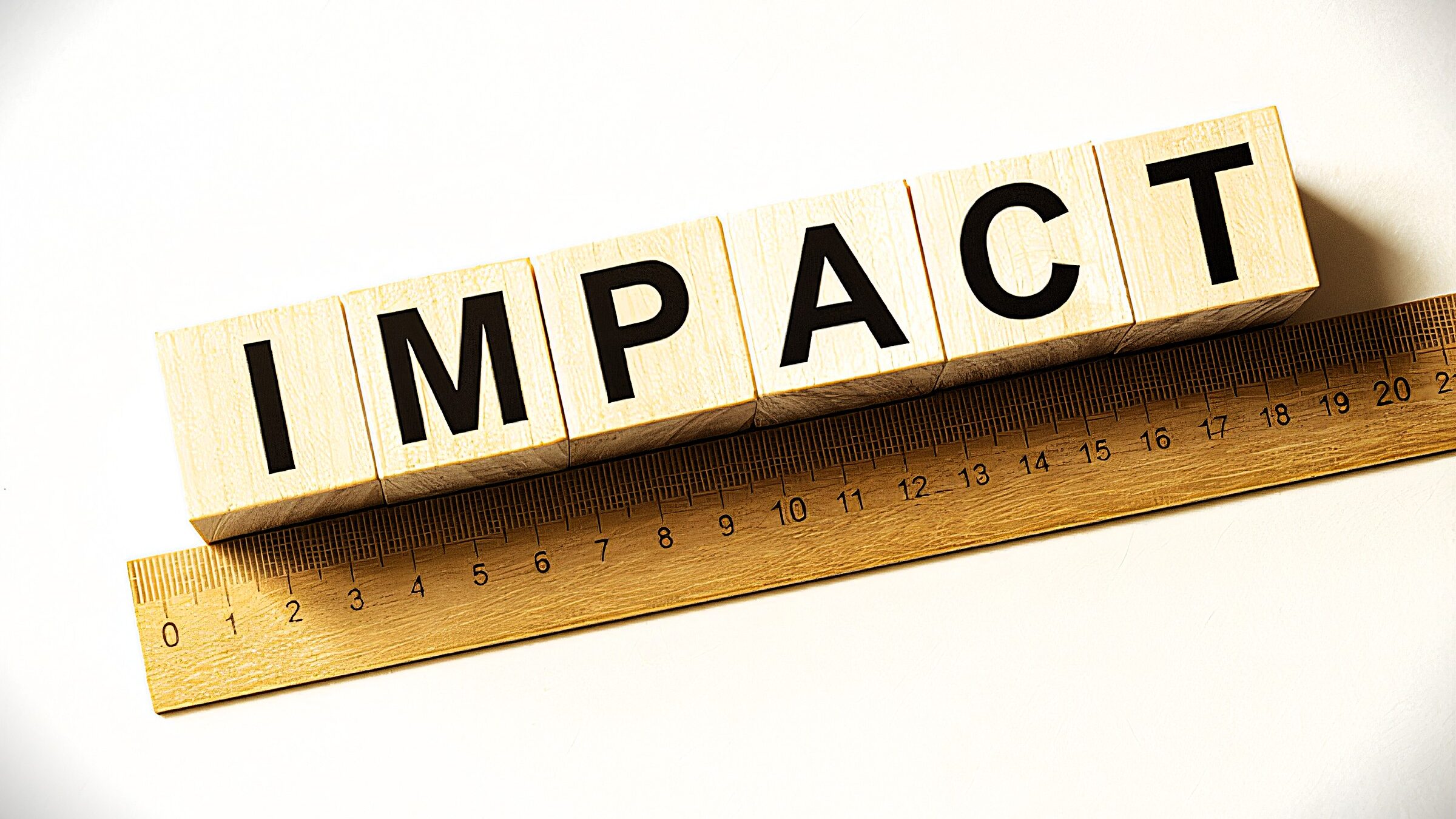 A set of wooden blocks spelling out "IMPACT" alongside a wooden ruler. This arrangement suggests the concept of measuring or quantifying impact.
